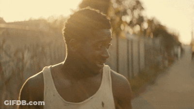 A Man Wearing A White Tank Top Is Walking Down A Road GIF