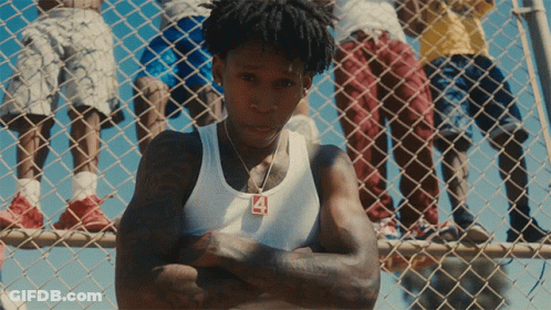 A Man Wearing A White Tank Top With The Number 4 On It Stands In Front Of A Chain Link Fence GIF