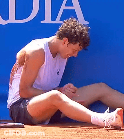 A Man Wearing A White Tank Top With The Word Oc On It Is Sitting On The Ground GIF