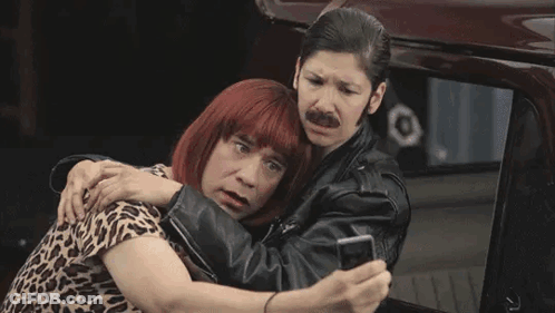A Man Wearing A Wig And A Leather Jacket Is Standing Next To Another Man Wearing A Leather Jacket . GIF