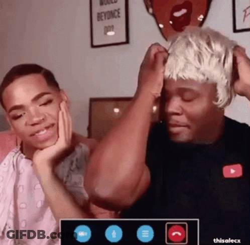 A Man Wearing A Wig Is Sitting Next To Another Man . GIF