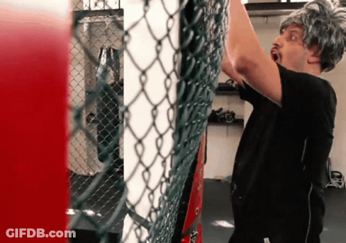 A Man Wearing A Wig Is Standing In Front Of A Chain Link Fence In A Gym GIF