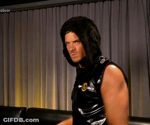 A Man Wearing A Wig Is Standing In Front Of A Curtain With The Word Eliver On The Bottom Right GIF