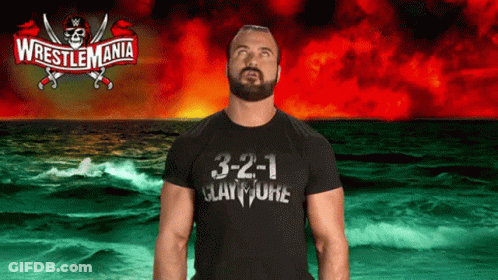 A Man Wearing A Wrestlemania T-Shirt Stands In Front Of A Stormy Ocean GIF