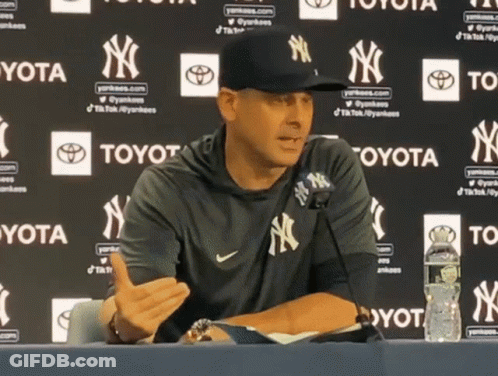 A Man Wearing A Yankees Hat Is Sitting At A Table GIF
