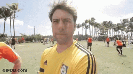 A Man Wearing A Yellow Adidas Shirt Stands In Front Of A Soccer Field GIF