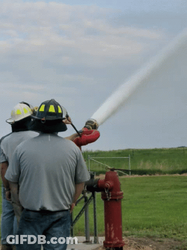 A Man Wearing A Yellow And Black Helmet Is Spraying Water From A Fire Hydrant GIF