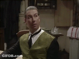 A Man Wearing A Yellow And Black Striped Vest And Tie Is Sitting At A Table GIF