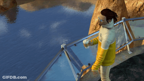 A Man Wearing A Yellow And White Sweatshirt With The Letter S On It Stands On A Bridge Overlooking A Body Of Water GIF