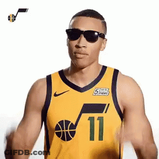 A Man Wearing A Yellow Basketball Jersey And Sunglasses Is Standing In Front Of A White Background . GIF