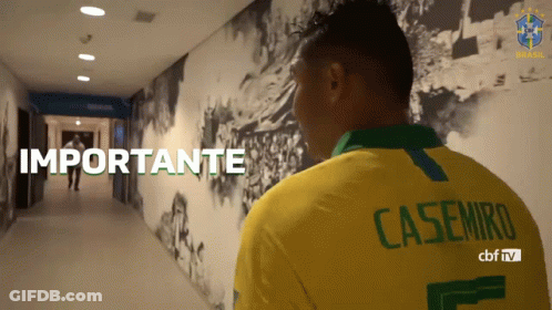 A Man Wearing A Yellow Casemiro Shirt Stands In A Hallway GIF