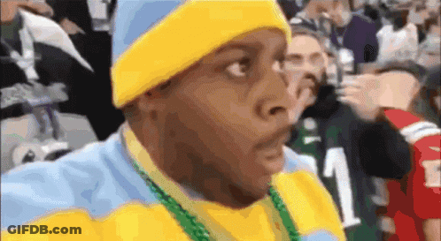 A Man Wearing A Yellow Hat And A Blue And Yellow Sweater With A Green Necklace Around His Neck GIF