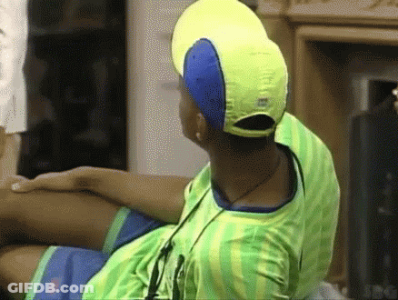 A Man Wearing A Yellow Hat And A Green Shirt Is Sitting On A Couch . GIF