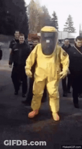 A Man Wearing A Yellow Hazmat Suit Is Walking Down The Street GIF