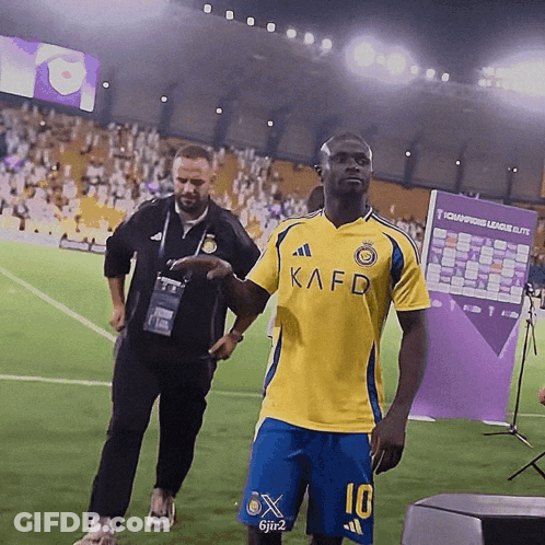 A Man Wearing A Yellow Kafd Shirt And Blue Shorts GIF