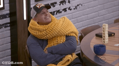 A Man Wearing A Yellow Scarf And A Hat Is Sitting At A Table GIF