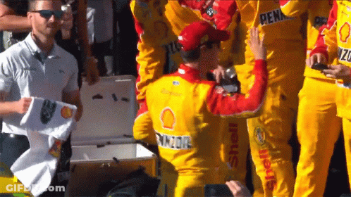 A Man Wearing A Yellow Shell Shirt Stands In A Crowd Of People GIF
