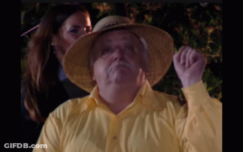 A Man Wearing A Yellow Shirt And A Straw Hat Is Being Kissed By A Woman GIF