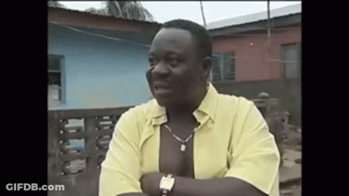 A Man Wearing A Yellow Shirt And A Watch Is Standing In Front Of A Building . GIF