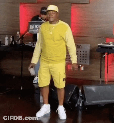 A Man Wearing A Yellow Shirt And Shorts Stands In Front Of A Dj Box GIF