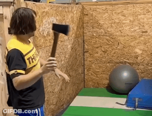 A Man Wearing A Yellow Shirt That Says This Is Holding An Axe In Front Of A Wooden Wall . GIF