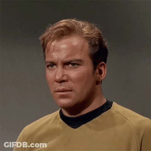 A Man Wearing A Yellow Shirt With A Black Collar Looks At The Camera GIF
