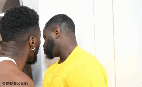 A Man Wearing A Yellow Shirt With The Letter C On It Stands Next To Another Man GIF