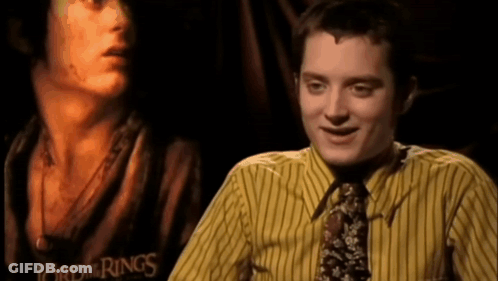 A Man Wearing A Yellow Striped Shirt And Tie Is Smiling In Front Of A Poster For The Lord Of The Rings GIF