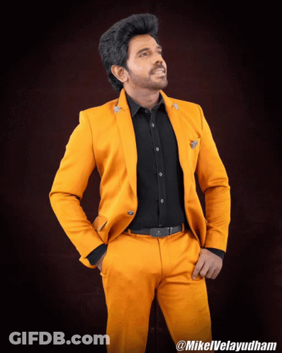 A Man Wearing A Yellow Suit And A Black Shirt Is Standing With His Hands In His Pockets And The Hashtag Mikelvelayudham GIF