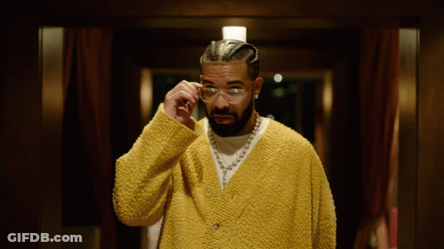 A Man Wearing A Yellow Sweater And Glasses Looks Down GIF