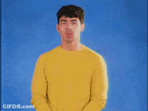 A Man Wearing A Yellow Sweater Stands In Front Of A Blue Background GIF