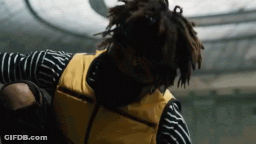 A Man Wearing A Yellow Vest And A Striped Shirt Is Standing On A Skateboard . GIF