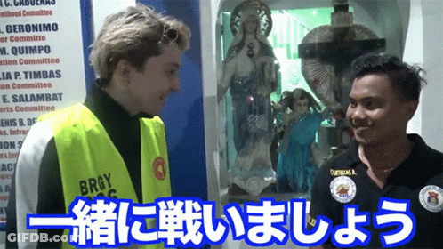 A Man Wearing A Yellow Vest That Says Brgy Is Talking To Another Man GIF