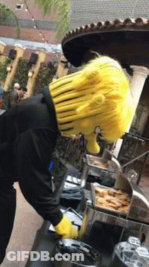 A Man Wearing A Yellow Wig And Yellow Gloves Is Standing In Front Of A Buffet Line GIF