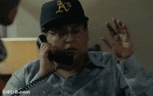 A Man Wearing An A 'S Hat Is Talking On A Telephone GIF