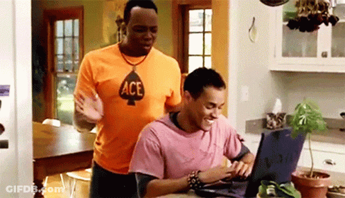 A Man Wearing An Ace Shirt Is Standing Next To Another Man Using A Laptop Computer GIF