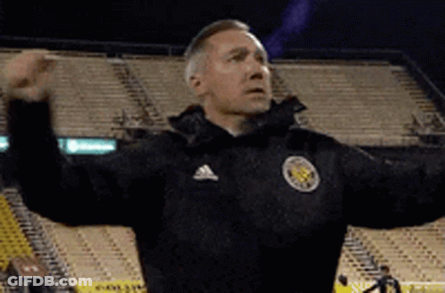 A Man Wearing An Adidas Jacket Is Standing In A Stadium With His Arms Outstretched . GIF