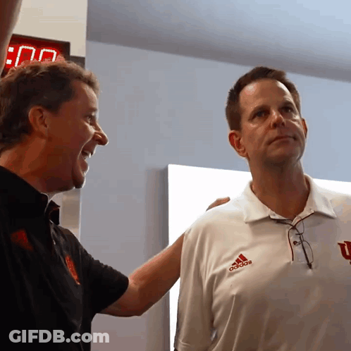 A Man Wearing An Adidas Shirt Stands Next To A Man Wearing A Black Shirt GIF