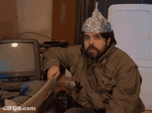 A Man Wearing An Aluminum Foil Hat Sits In A Bin GIF