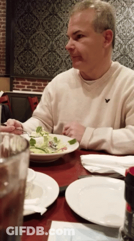 A Man Wearing An American Eagle Sweater Sits At A Table GIF
