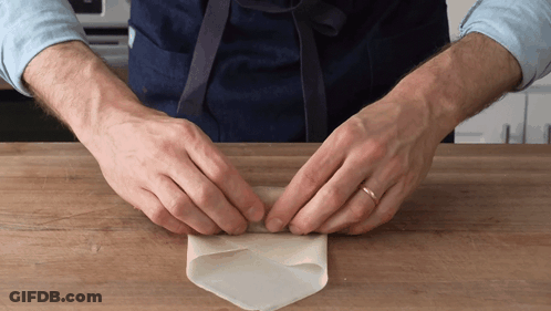 A Man Wearing An Apron Is Folding A Piece Of Paper GIF