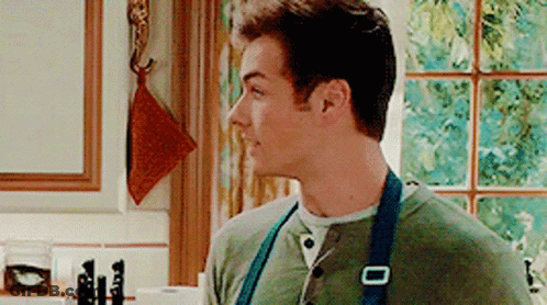 A Man Wearing An Apron Is Standing In A Kitchen . GIF