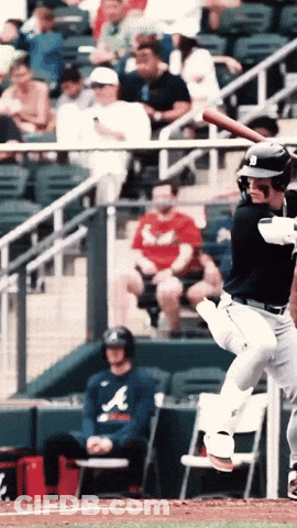 A Man Wearing An Atlanta Shirt Sits In The Dugout Watching A Baseball Player Swing His Bat GIF