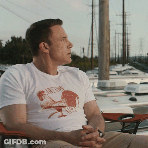A Man Wearing An Awesome Sauce Shirt Sits On A Chair GIF