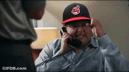 A Man Wearing An Indians Hat Is Talking On A Telephone GIF