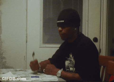 A Man Wearing An Oakley Hat Sits At A Table With A Spoon In His Hand GIF