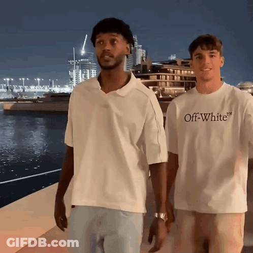 A Man Wearing An Off White T-Shirt Is Standing Next To Another Man GIF