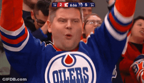 A Man Wearing An Oilers Jersey Holds Up His Arms In The Air GIF