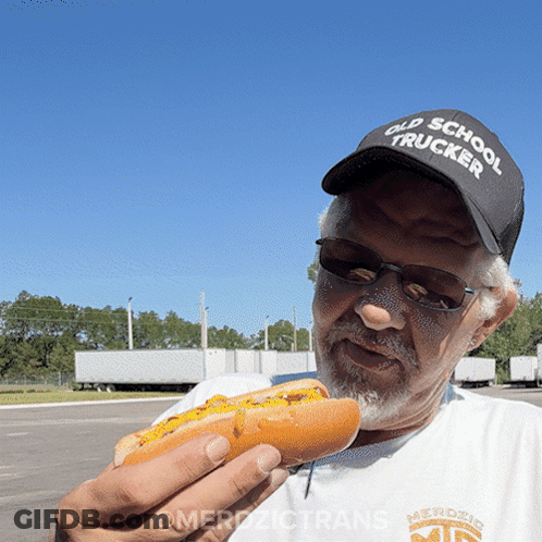 A Man Wearing An Old School Trucker Hat Eats A Hot Dog GIF