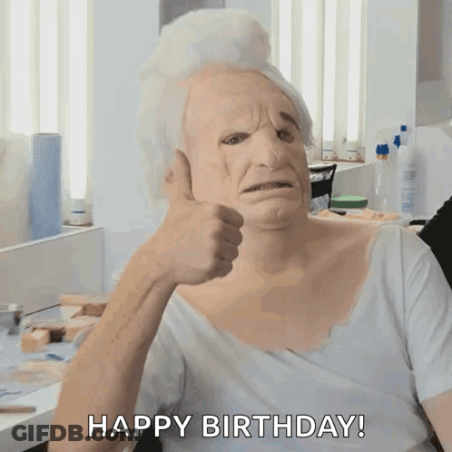 A Man Wearing An Old Woman 'S Mask Giving A Thumbs Up With The Words Happy Birthday Behind Him GIF